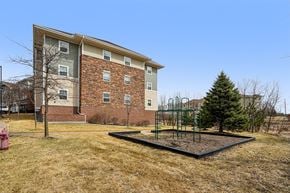 Forest Lake apartment for rent - A playground with a swing set in front of a brick apartment building.