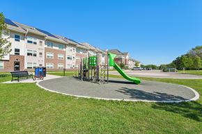 Faribault apartment for rent - A playground with a green slide and a bench in front of apartment buildings.