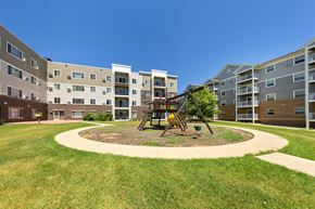 Rochester apartment for rent - A playground with a swing set is in the middle of a grassy area in front of apartment buildings.