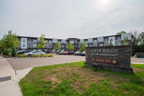 Waconia apartment for rent - A sign for Vista Ridge stands in front of a parking lot and apartment building.