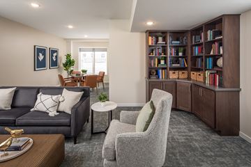 Burnsville apartment for rent - A living room with a grey sofa, a grey armchair, a coffee table, and a bookshelf filled with books.