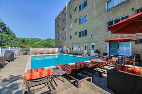Pittsburgh apartment for rent - A pool area with chairs and umbrellas in front of a building.