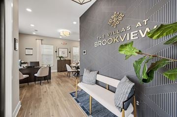 Brook Park apartment for rent - A living room with a couch and a plant in front of a wall with a sign that says "Villas at Brookview".