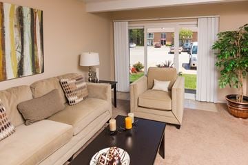 North Olmsted apartment for rent - A living room with a beige couch, a chair, a table with a candle, and a painting on the wall.