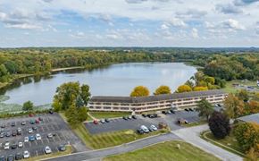 Stow apartment for rent - A large building is situated next to a parking lot with a lake in the background.