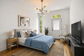Brooklyn apartment for rent - A bedroom with a bed, a chair, a lamp, a plant, and a television.