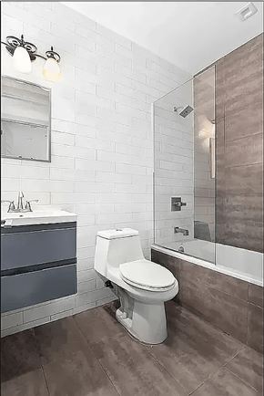 Brooklyn apartment for rent - A white toilet sits in a bathroom with a white and brown tile wall.