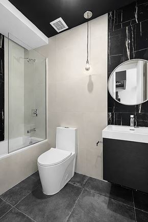 Brooklyn apartment for rent - A white toilet sits in a bathroom with a black and white tiled wall.