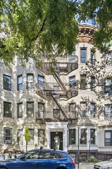 Brooklyn apartment for rent - A blue car is parked on the street in front of a building with a fire escape.