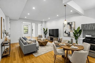 Brooklyn apartment for rent - A modern living room with a grey sofa, a wooden coffee table, and a dining table set for six.