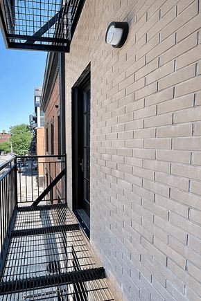 Brooklyn apartment for rent - A brick wall with a black gate and a small square light fixture on it.