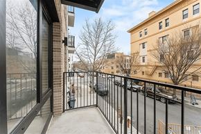 Brooklyn apartment for rent - A balcony with a black railing and a view of a parking lot and buildings.