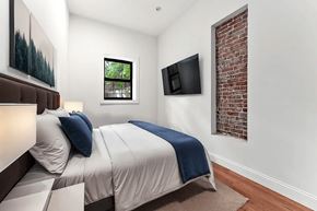 Brooklyn apartment for rent - A bedroom with a bed, a window, a painting, a flat screen TV and a brick wall.