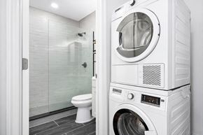 Brooklyn apartment for rent - A white washing machine is in a bathroom with a toilet and glass shower door.