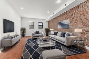 Brooklyn apartment for rent - A living room with a grey couch, a black television, and a brick wall.