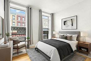 Brooklyn apartment for rent - A bedroom with a large bed, a chair, and a window overlooking a balcony.
