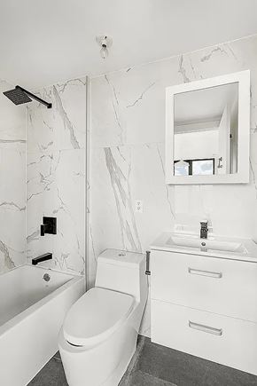 Brooklyn apartment for rent - A white bathroom with a marble wall and a round toilet.