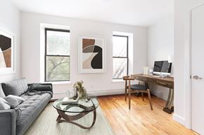 Brooklyn apartment for rent - A modern living room with a grey couch, a glass coffee table, and a wooden desk with a laptop.