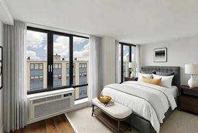 Brooklyn apartment for rent - A bedroom with a large bed, a window with a view of a cityscape, and a nightstand with a lamp.