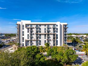 Aventura apartment for rent - A large white building with balconies is surrounded by trees and a parking lot.