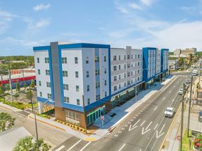 Bradenton apartment for rent - A modern multi-story building with blue and white exterior is situated on a street corner with cars parked along the curb.
