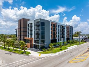 Deerfield Beach apartment for rent - A modern multi-story building with a parking lot in front.