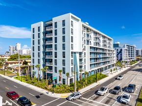 Hollywood apartment for rent - A modern white apartment building is situated on a street corner with cars parked and driving by.