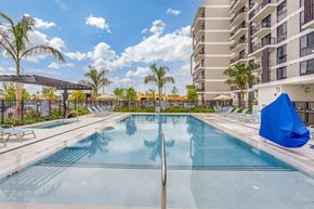 Palmetto Bay apartment for rent - A large swimming pool in front of a building with a blue umbrella on the right side.