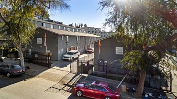 Los Angeles apartment for rent - A red car is parked in front of a building with a black fence.