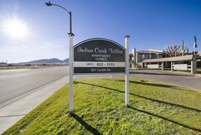 Tehachapi apartment for rent - A sign for Indian Creek Village Apartment Homes stands on a grassy area by a road.