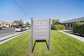 Hemet apartment for rent - A sign for Kidby Gardens Apartments stands in the grass by a road.