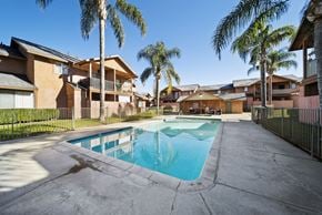 Hemet apartment for rent - A swimming pool surrounded by palm trees and apartment buildings.