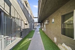 North Hills apartment for rent - A long, narrow walkway between two buildings with grass on the ground.