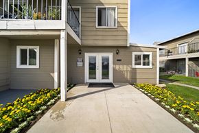 San Bernardino apartment for rent - A building with a white door and windows with flower beds in front.