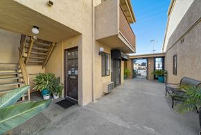 Van Nuys apartment for rent - A sunny day at the entrance of a building with a bench and potted plants.