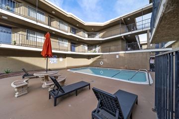 Canoga Park apartment for rent - A pool area with a red umbrella and black lounge chairs.