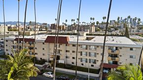 Los Angeles apartment for rent - A view of a residential building with cars parked in front and palm trees in the foreground.