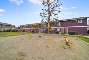 Avenal apartment for rent - A playground with a yellow swing set and a red slide in front of a red building.