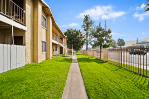 San Bernardino apartment for rent - A long concrete walkway leads to a building with a metal fence on one side and a grassy area on the other.