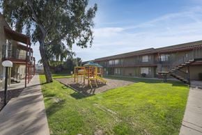 Phoenix apartment for rent - A playground with a slide and swings is surrounded by grass and trees.