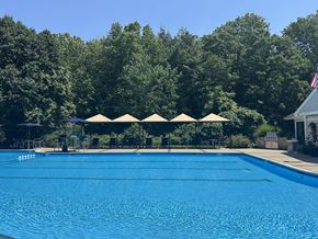 Andover apartment for rent - A large blue swimming pool surrounded by trees and umbrellas.