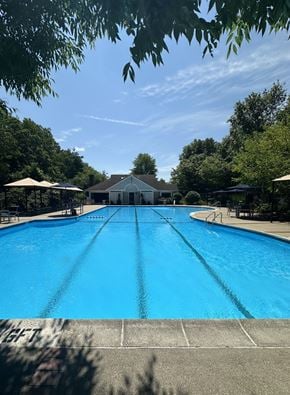 Andover apartment for rent - A large blue swimming pool surrounded by trees and a building in the background.