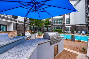A blue umbrella shades a table and chairs on a patio.
