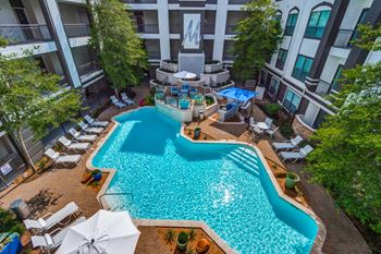 A swimming pool surrounded by lounge chairs and umbrellas in a courtyard.
