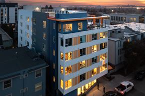 Berkeley apartment for rent - A tall building with a blue and white facade stands in the foreground of a cityscape at dusk.