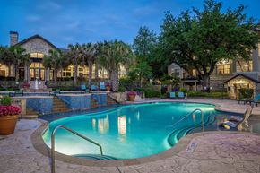 Austin apartment for rent - A swimming pool surrounded by a stone patio and a house with a lit up entrance.
