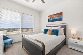 Aurora apartment for rent - A bedroom with a large bed, a blue chair, and a ceiling fan.