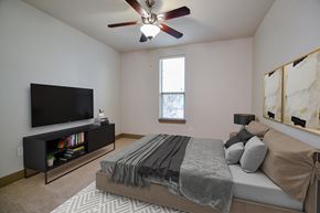 Dallas apartment for rent - A bedroom with a bed, a television, and a ceiling fan.
