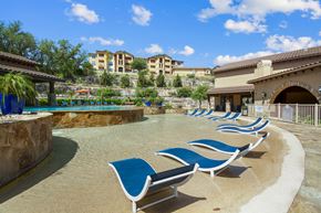 San Antonio apartment for rent - A pool area with blue lounge chairs and a stone wall.