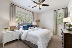 Charlotte apartment for rent - A bedroom with a large bed, a ceiling fan, and a nightstand with a plant on it.